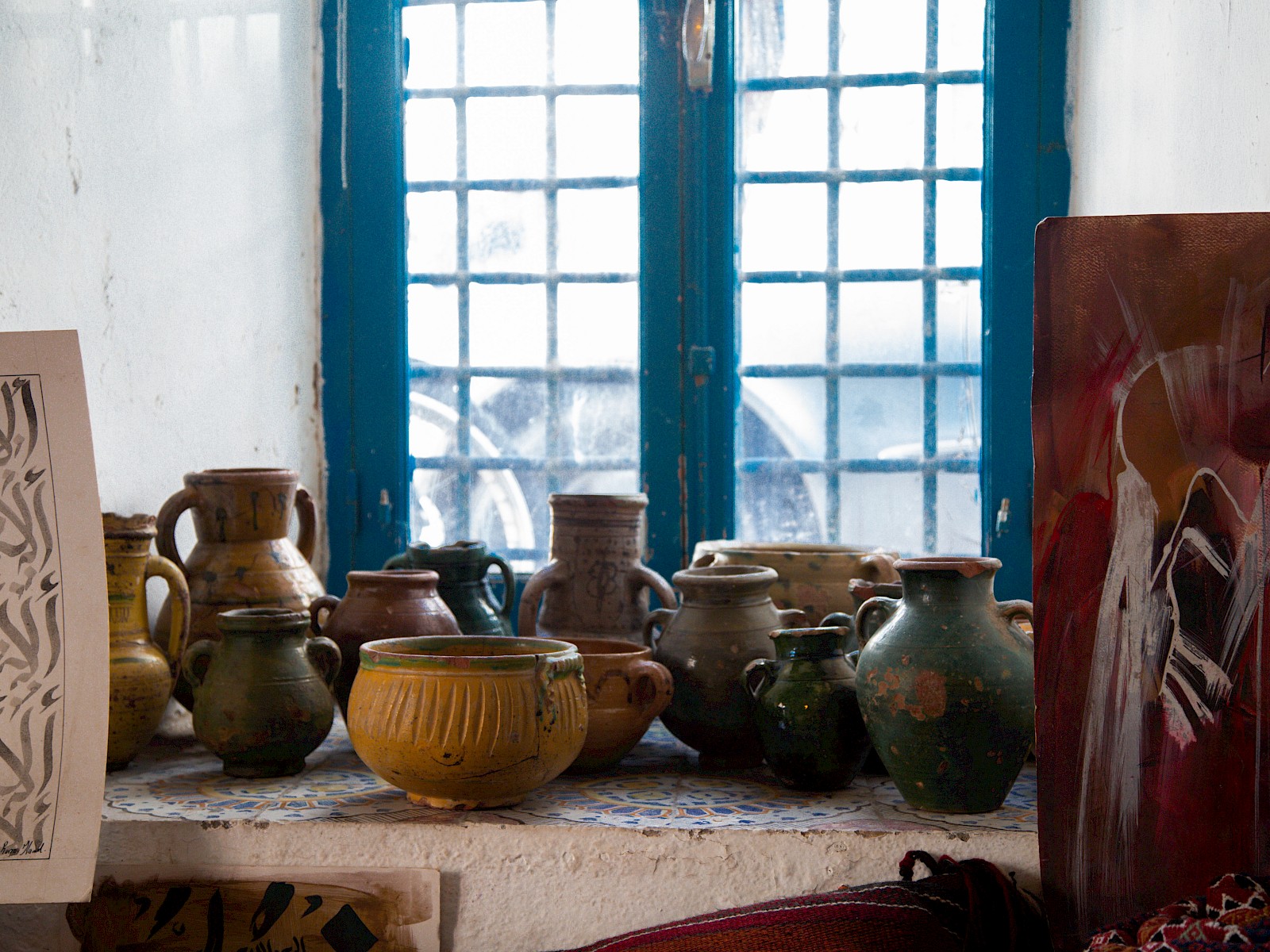 Close-up of a bright blue window and handmade crafts, with two paintings on the sides.