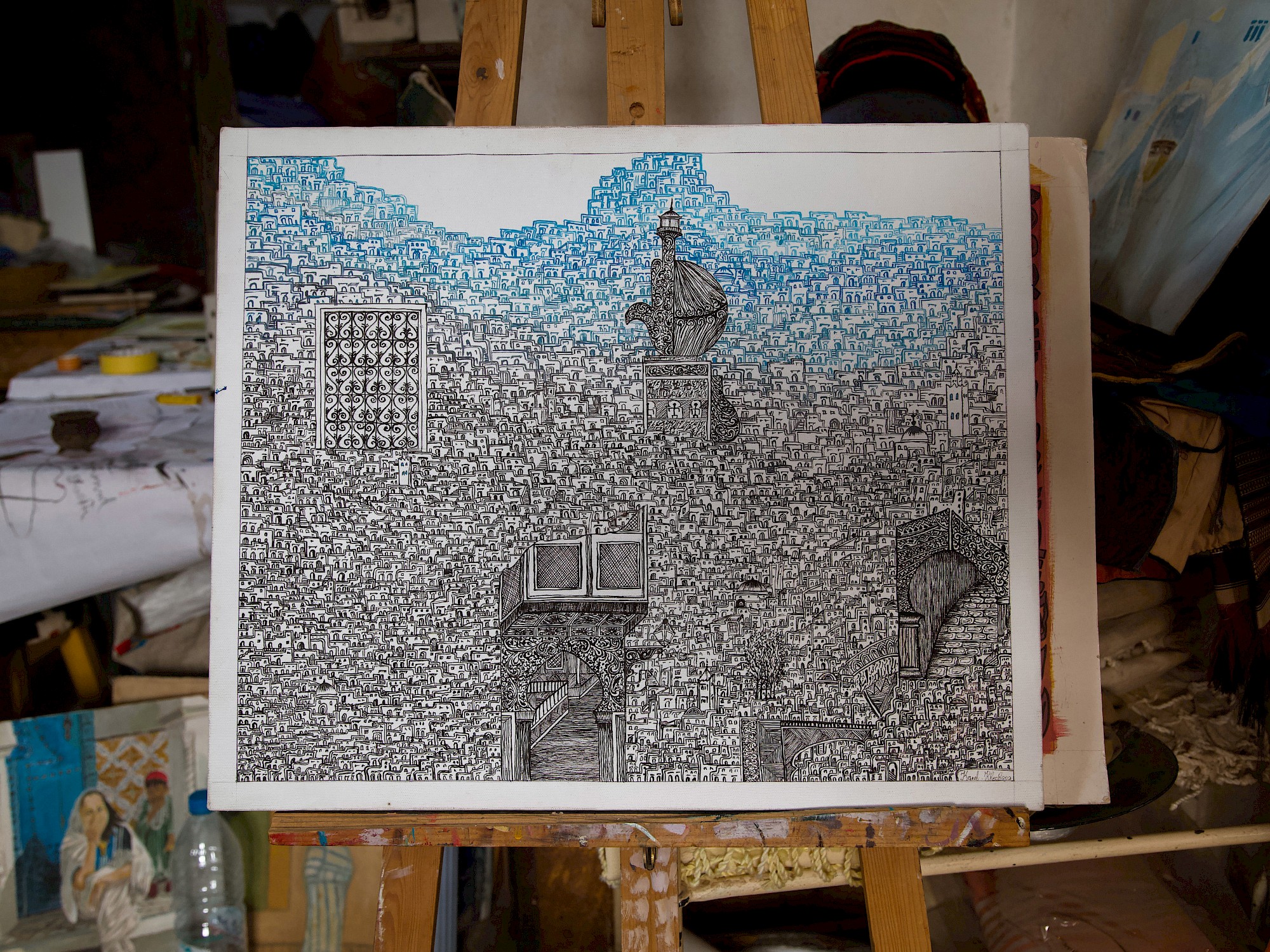 A detailed black-and-white ink drawing of a dense hillside town, with vertical blue shapes rising through its centre, resting on an easel.